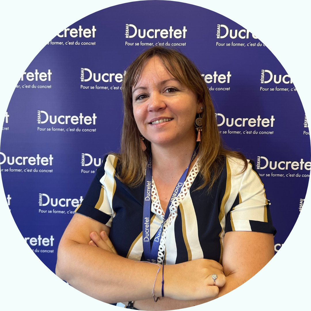 Femme, bras croisés, souriante, devant un décor Ducretet. Elle porte un haut rayé et un cordon.