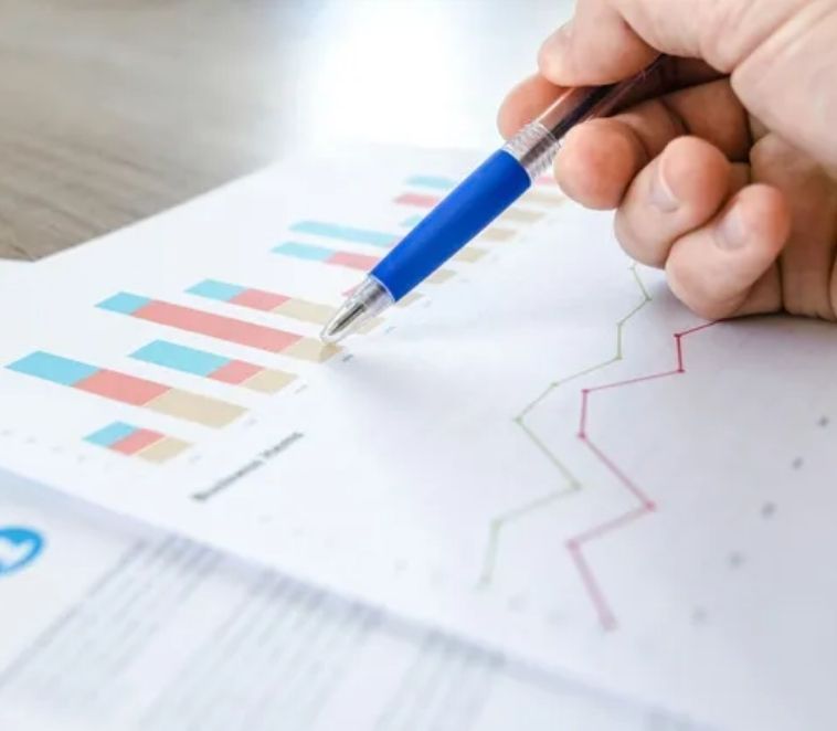 Main tenant un stylo bleu pointant du doigt des graphiques et des tableaux d'affaires sur papier.