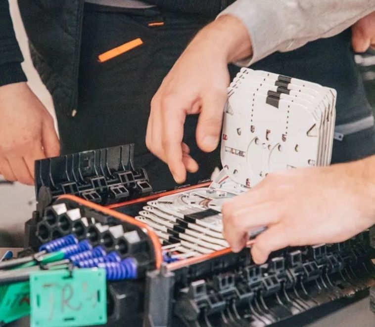 Deux personnes travaillent sur un circuit imprimé noir et blanc, connectant des fils et des câbles.