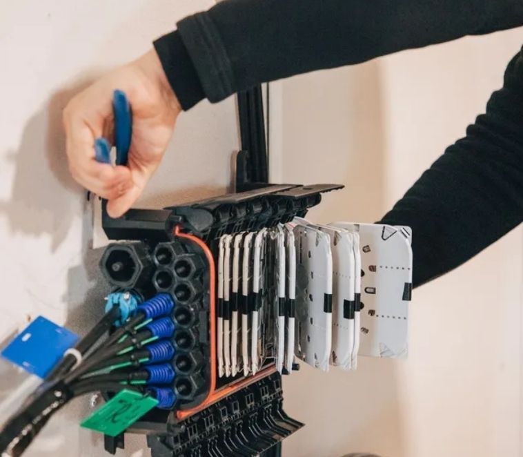 Une personne travaille sur un boîtier de distribution de câbles à fibres optiques mural avec des câbles bleus et verts.