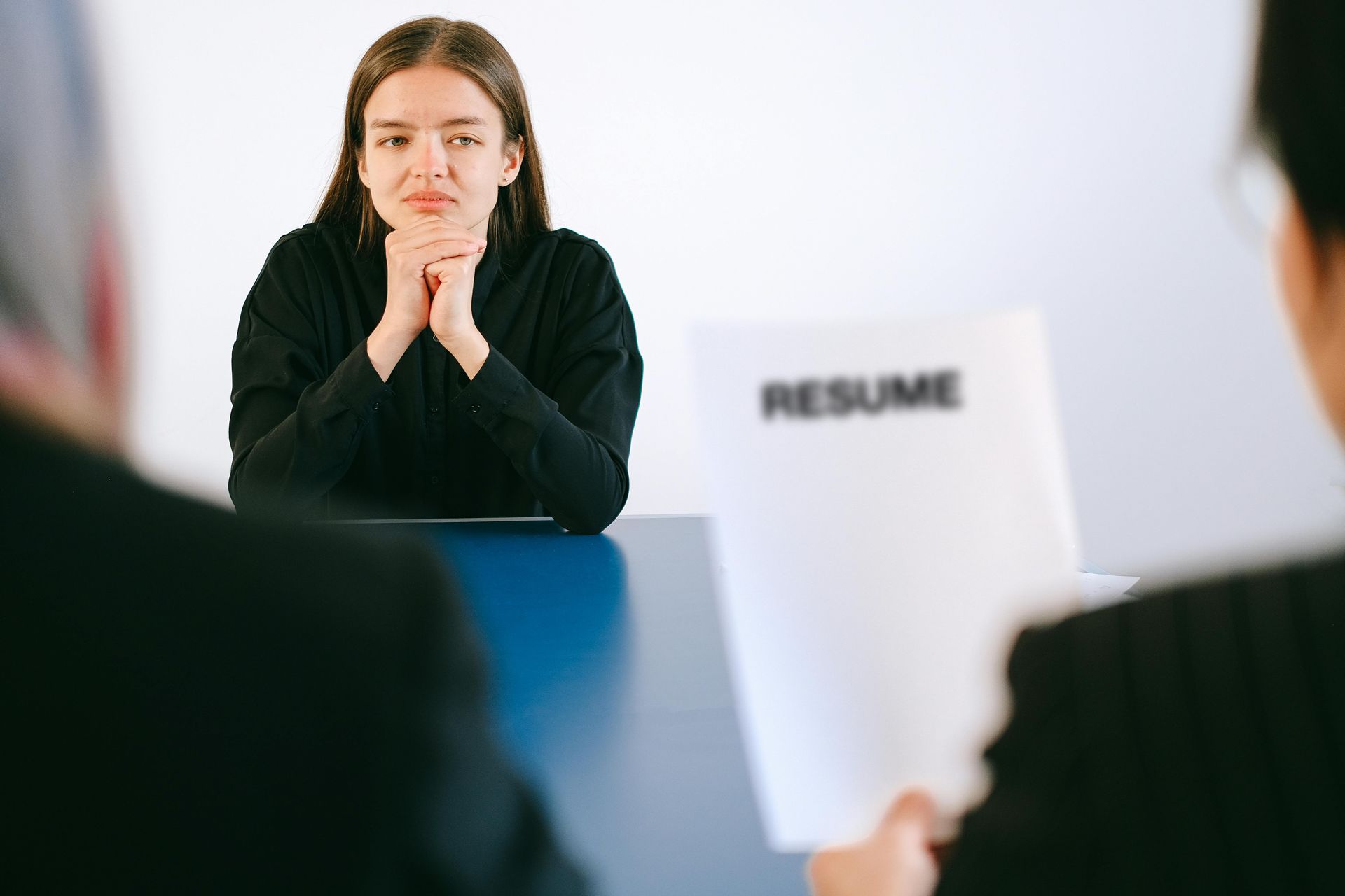 Une femme, assise à une table pour un entretien d'embauche, l'air sérieux, les mains jointes. Quelqu'un tient son CV.