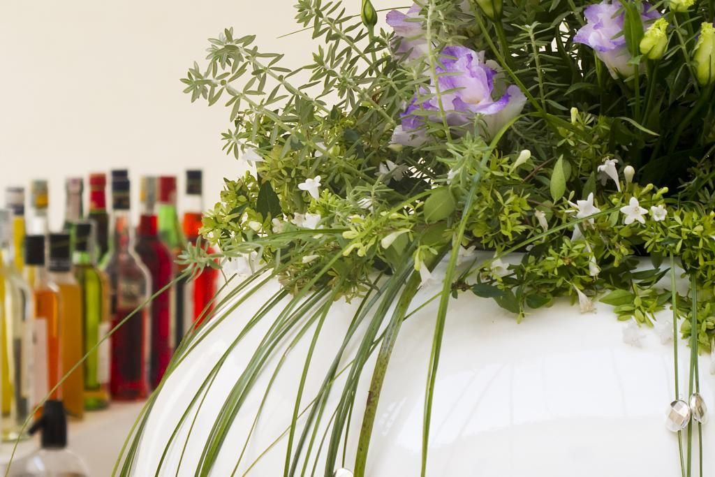 Su un tavolo accanto a bottiglie di liquore è posato un vaso pieno di fiori.