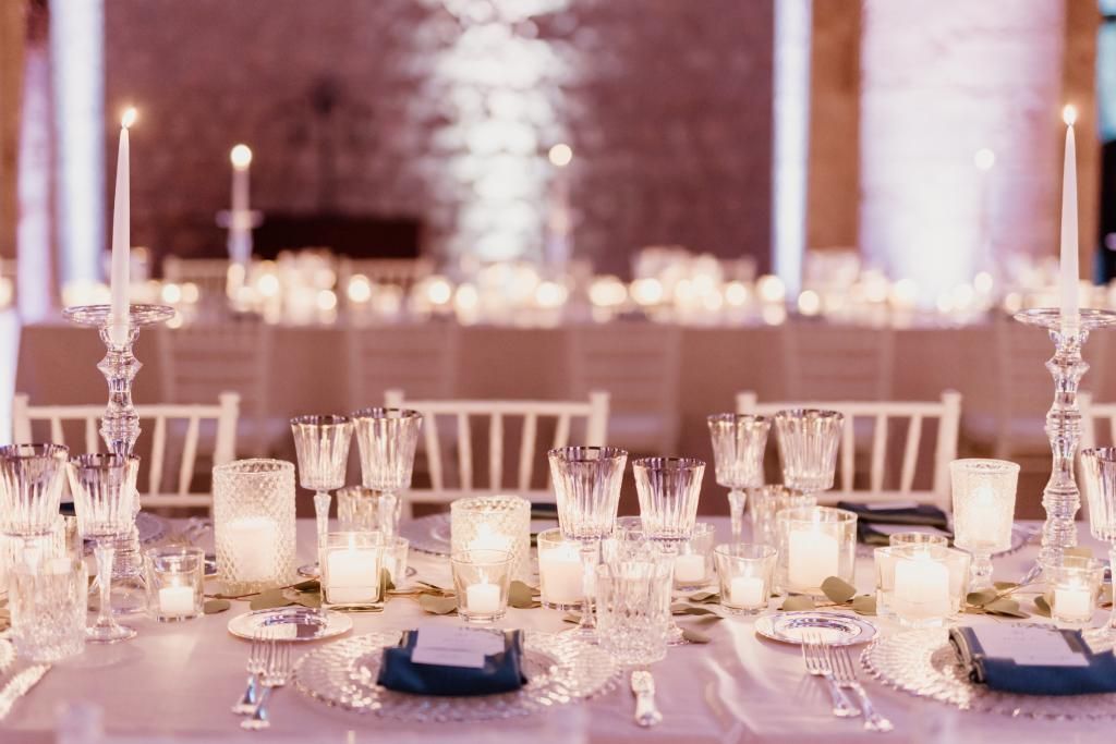 Un lungo tavolo apparecchiato per un ricevimento di nozze con candele e bicchieri.