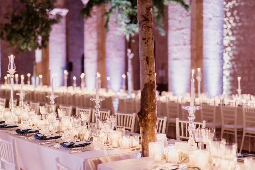 Un lungo tavolo apparecchiato per un ricevimento di nozze con candele e un albero al centro.