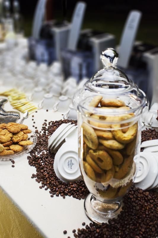 Un barattolo di vetro pieno di biscotti è posto su un tavolo circondato da chicchi di caffè