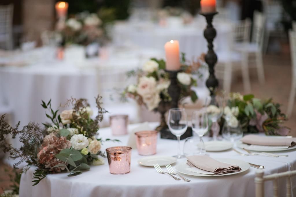 Una tavola apparecchiata per un ricevimento di nozze con candele e fiori sopra.