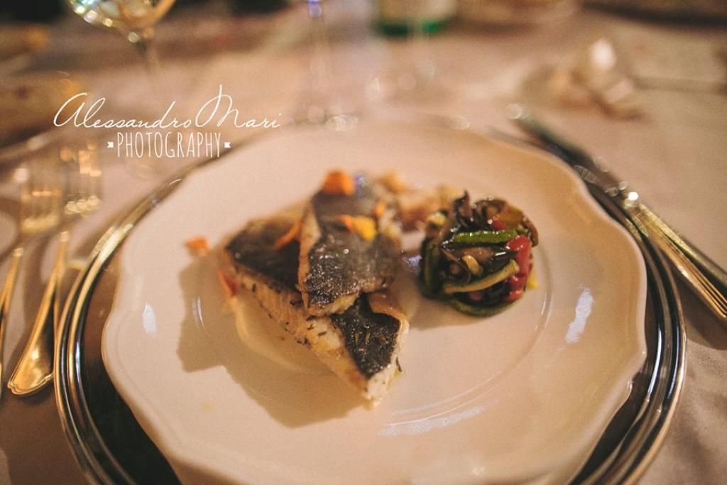 Un piatto bianco sormontato da un pezzo di pesce e verdure su un tavolo.