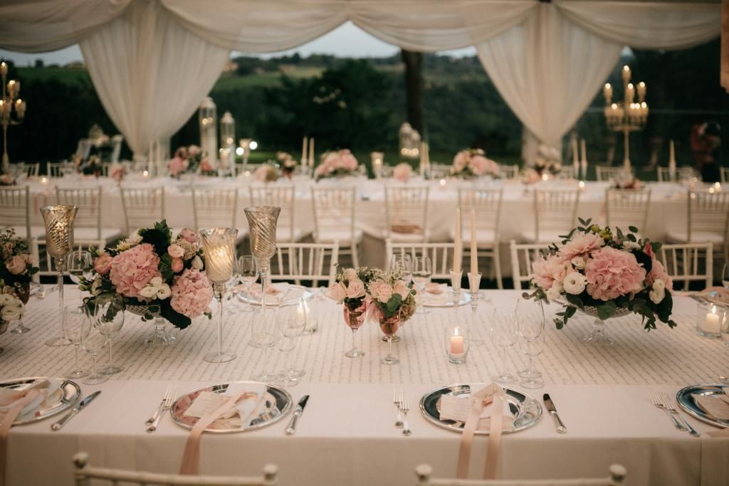 Un lungo tavolo con sopra piatti, candele e fiori.