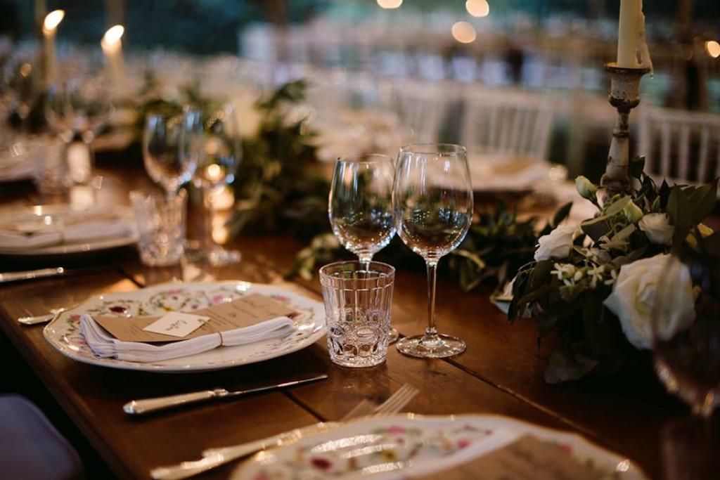 Una tavola apparecchiata per un ricevimento di nozze con piatti, bicchieri da vino e candele.