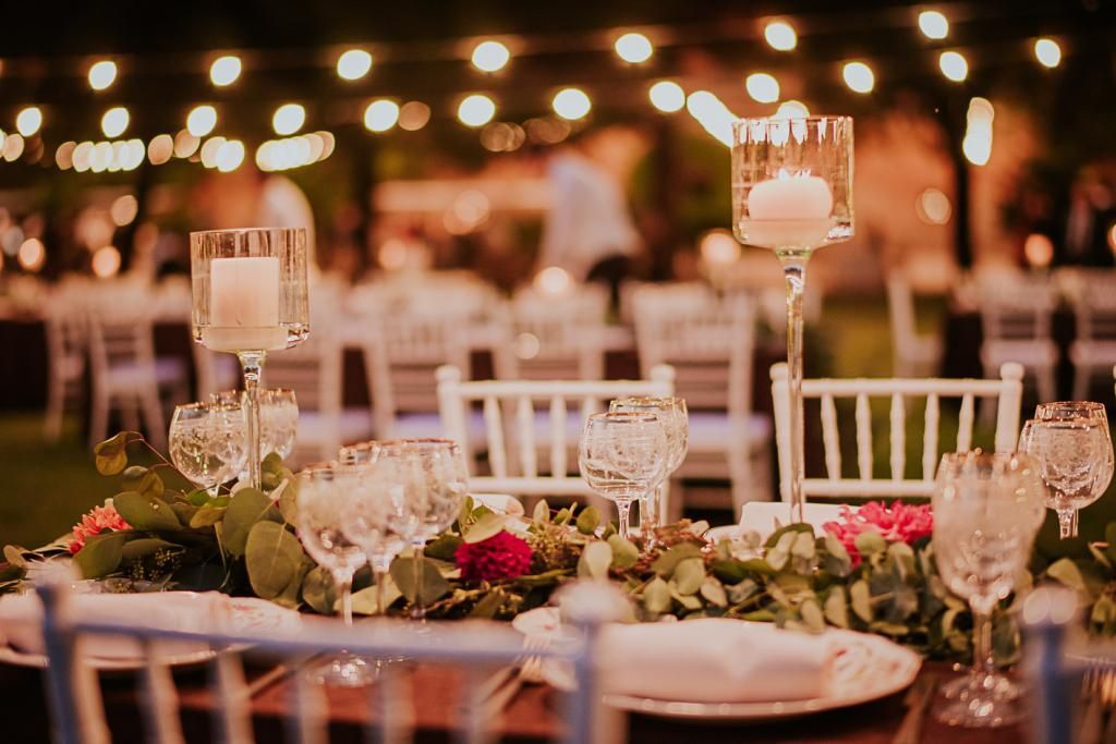 Una tavola apparecchiata per un ricevimento di nozze con piatti, bicchieri, candele e fiori.