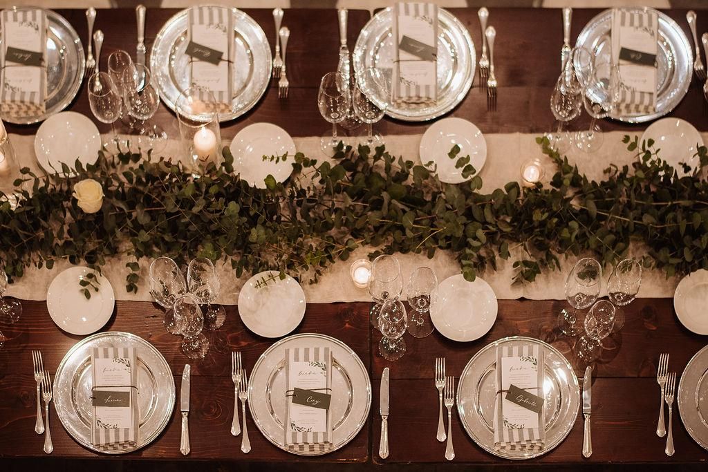 Un lungo tavolo di legno con piatti, posate, candele e una ghirlanda.