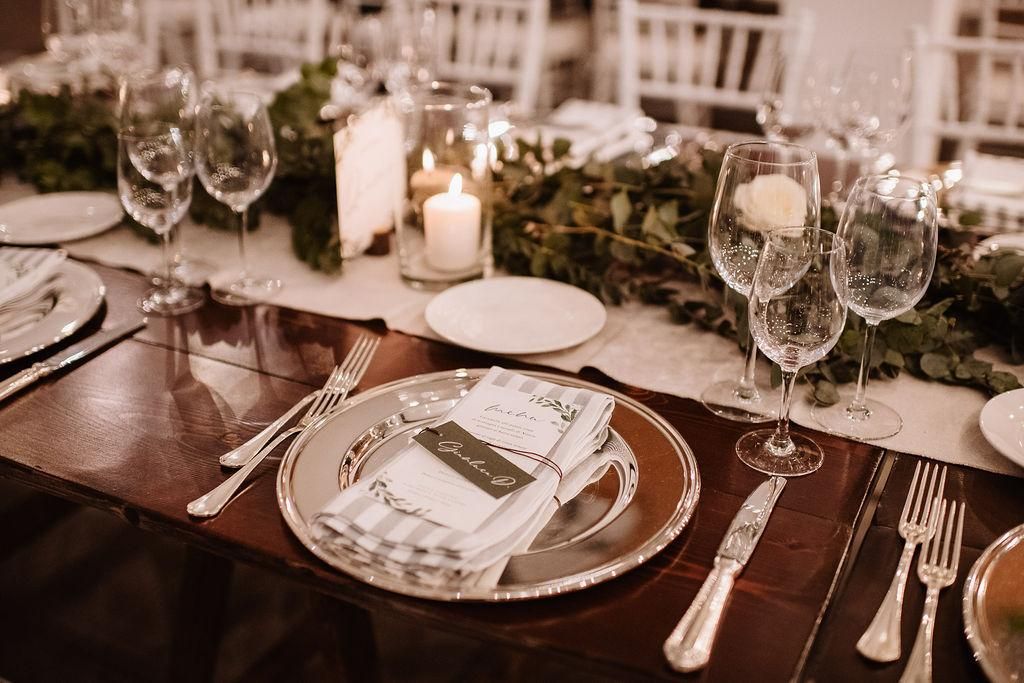 Una tavola apparecchiata per un ricevimento di nozze con piatti, bicchieri, candele e posate.