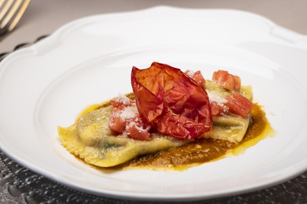 Un piatto bianco sormontato da un pezzo di cibo e pomodori