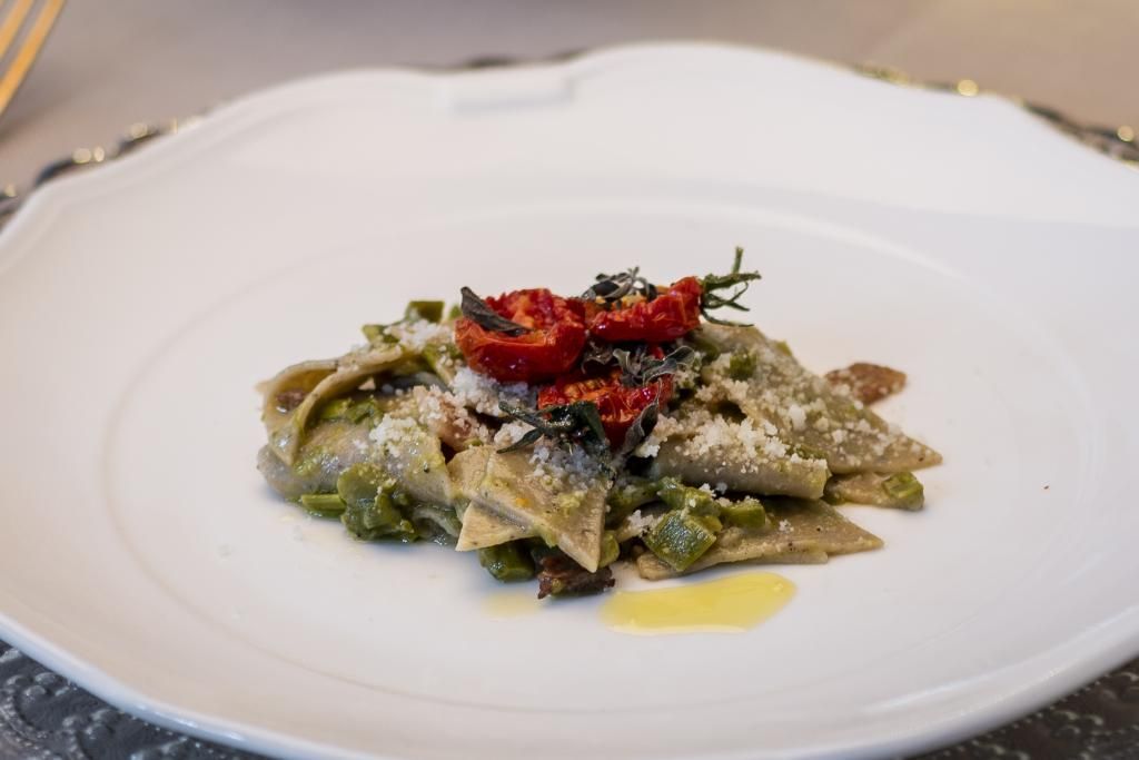 Un piatto bianco condito con pasta e pomodori su un tavolo.