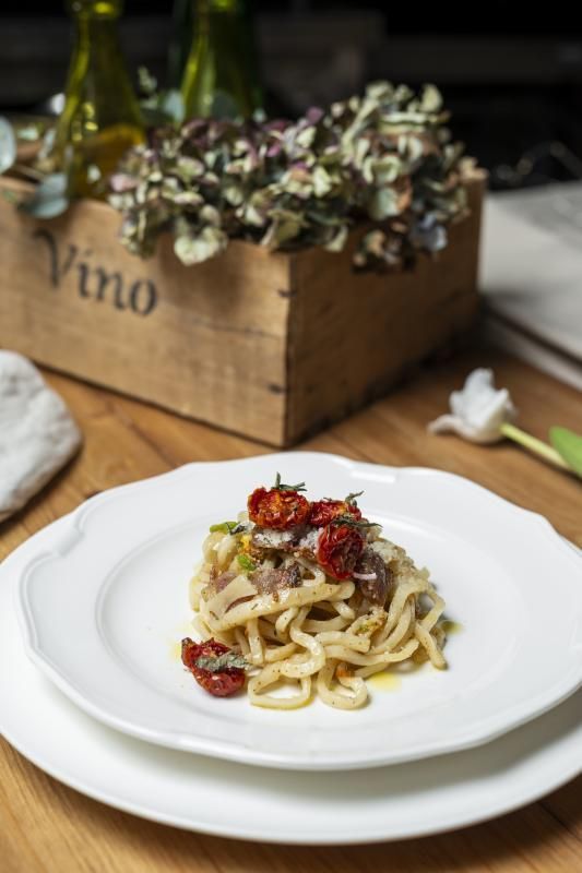 Un piatto bianco condito con tagliatelle e pomodori su un tavolo di legno.