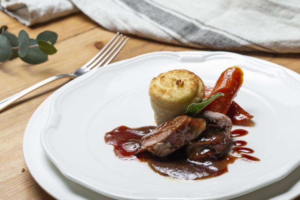 Un piatto bianco condito con carne e salsa su un tavolo di legno.