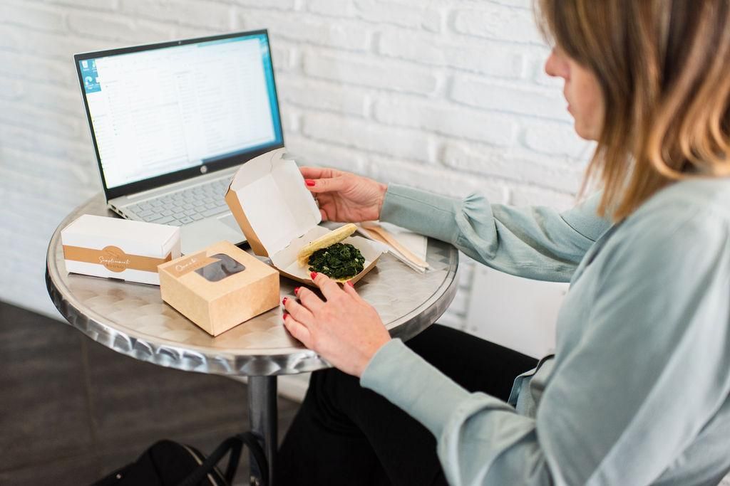 Una donna è seduta a un tavolo con un laptop e una scatola di cibo.