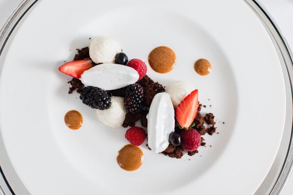 Un piatto bianco con frutti di bosco e cioccolato su un tavolo.