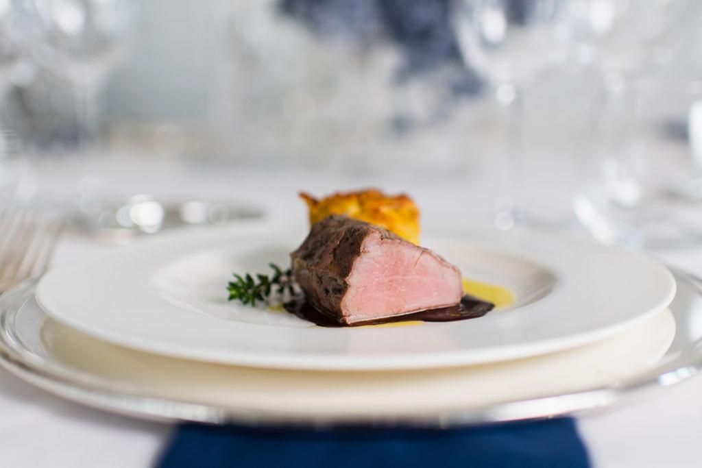 Un piatto bianco sormontato da un pezzo di carne su un tavolo.