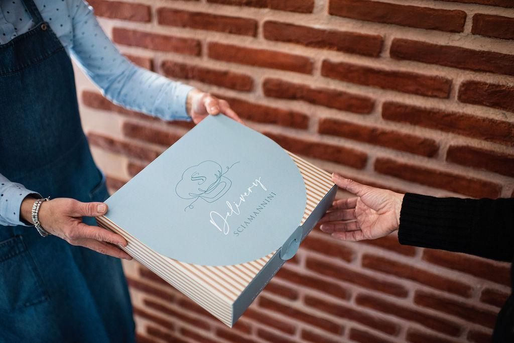 Una donna regala una scatola a un'altra donna davanti a un muro di mattoni.