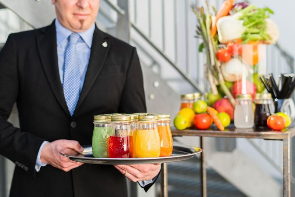 Un uomo in giacca e cravatta tiene in mano un vassoio con barattoli di succo.
