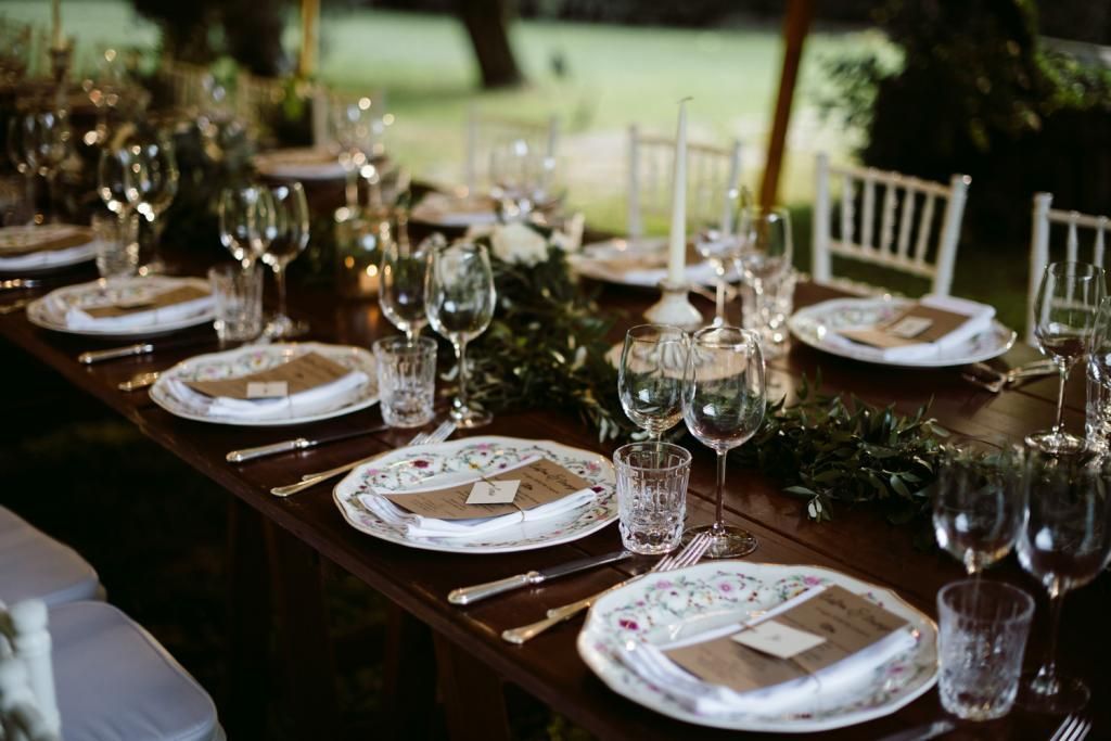 Un lungo tavolo di legno con piatti, bicchieri e posate per un ricevimento di nozze.