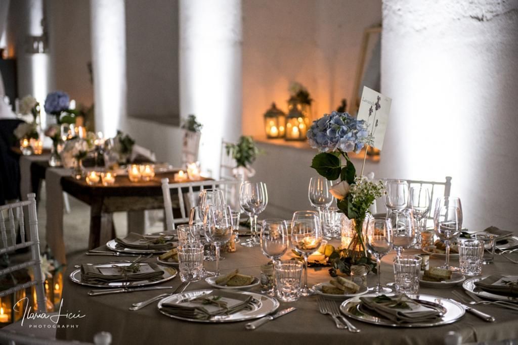 Una tavola apparecchiata per un ricevimento di nozze con piatti, bicchieri e candele.