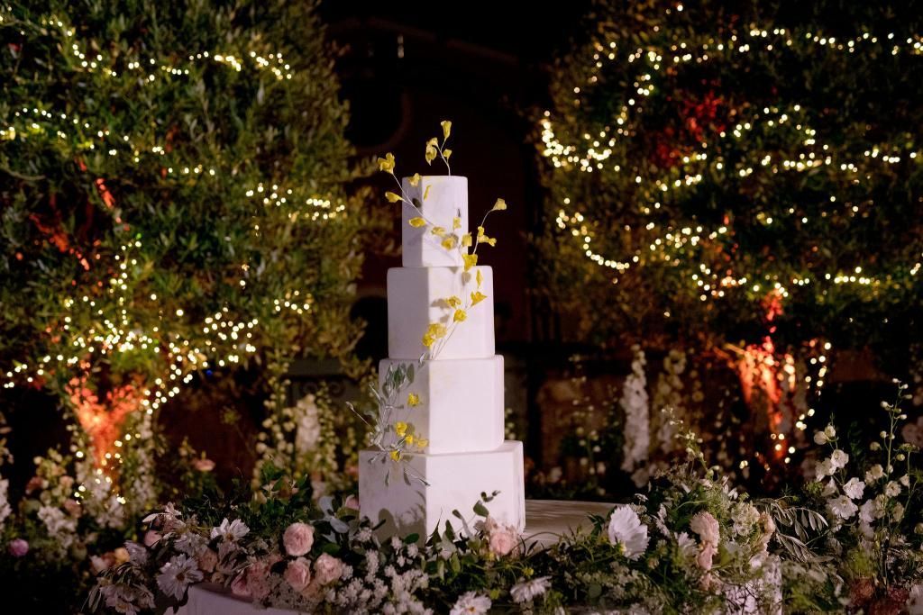 Su un tavolo circondato da fiori e luci è posata una torta nuziale.