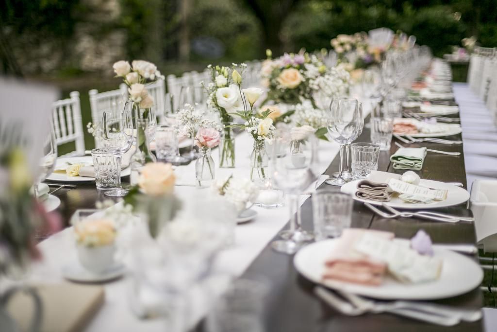 Un lungo tavolo con sopra piatti, bicchieri e fiori.