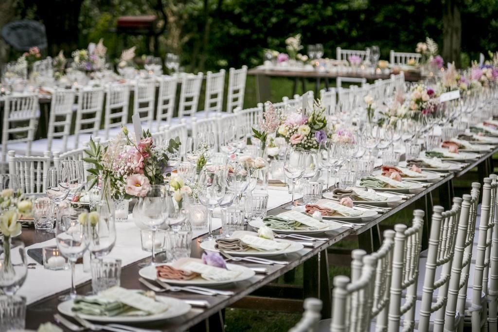 Un lungo tavolo con sopra piatti, bicchieri e fiori.