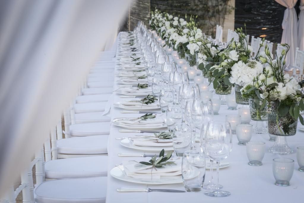 Un lungo tavolo con sopra piatti, bicchieri e vasi di fiori.