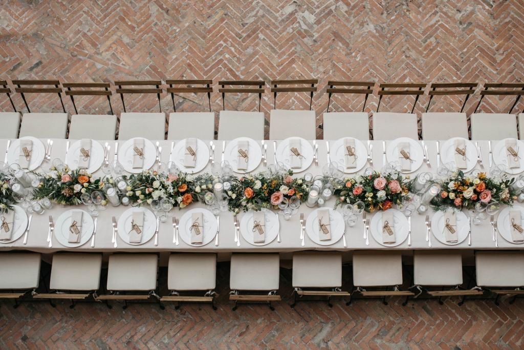 Un lungo tavolo con sopra piatti, bicchieri e fiori.