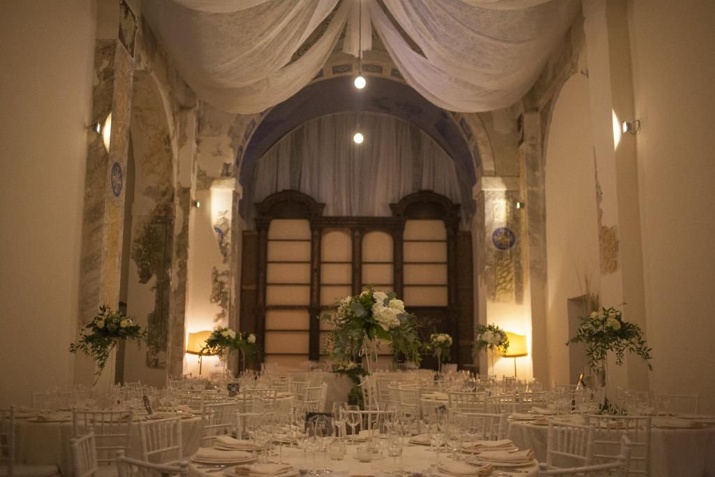 Un'ampia sala con tavoli e sedie allestita per un ricevimento di matrimonio.