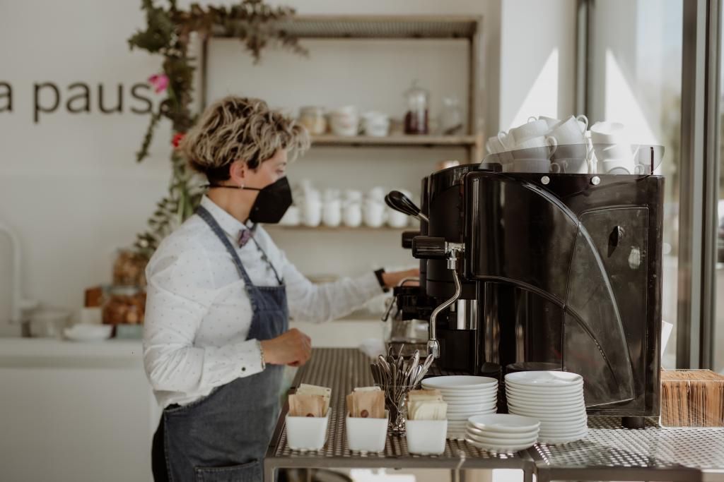 Una donna che indossa una maschera sta preparando il caffè in un ristorante.