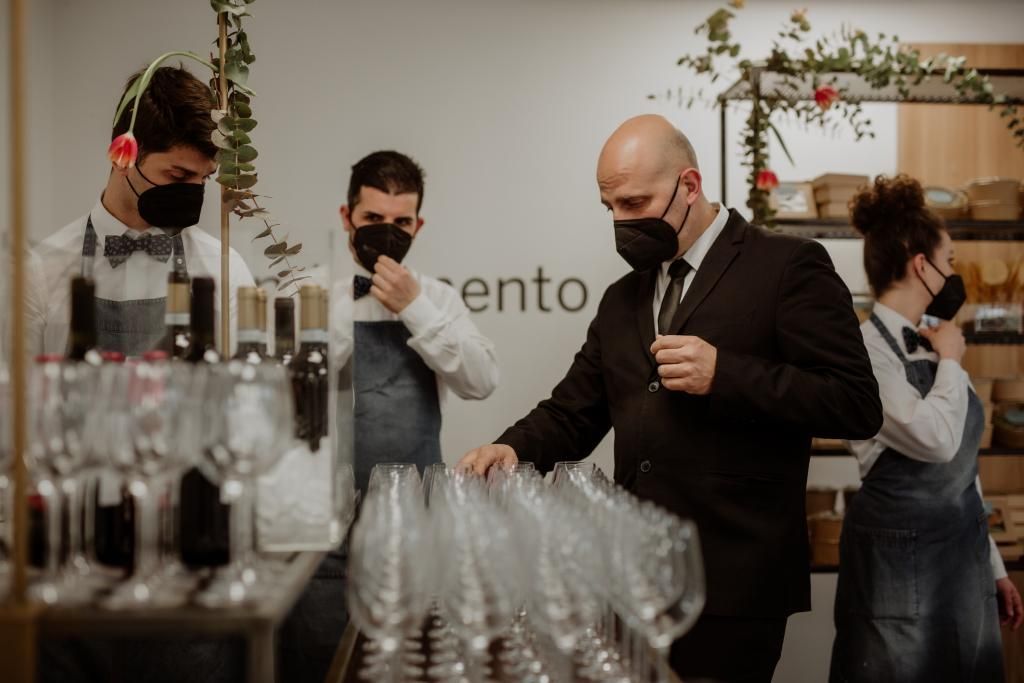 Un gruppo di persone che indossano maschere per il viso sono in piedi attorno a un tavolo con bicchieri di vino.