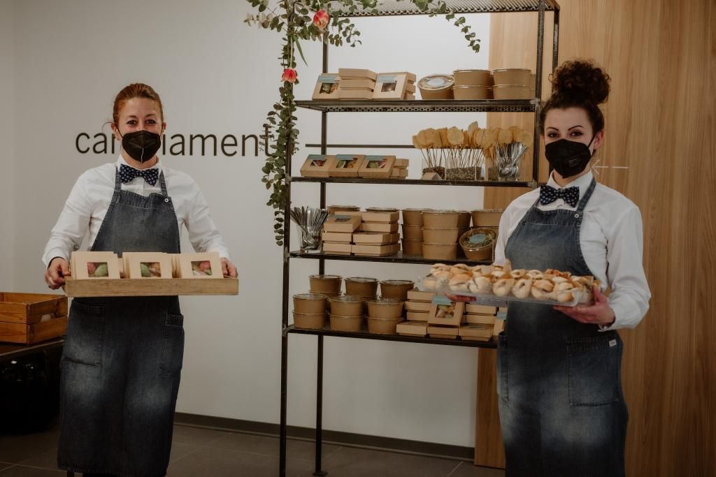 Due donne che indossano maschere per il viso tengono in mano vassoi di cibo.