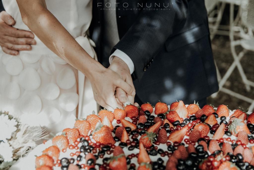 Una sposa e uno sposo stanno tagliando una torta nuziale con fragole e mirtilli.