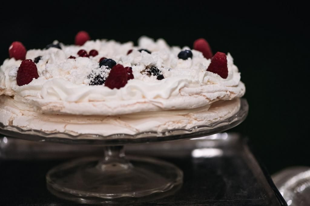 Su una lastra di vetro c'è una torta con panna montata e frutti di bosco in cima.