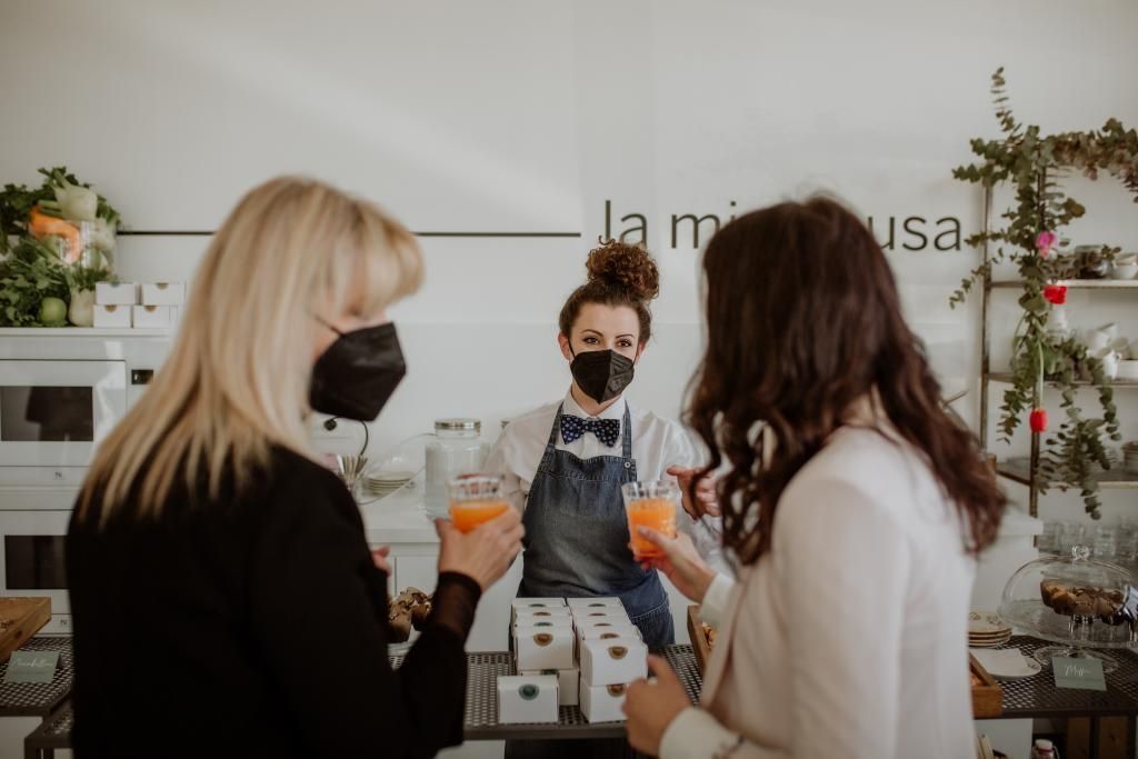 Una donna mascherata serve da bere a due donne.