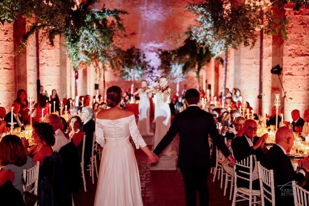 Una sposa e uno sposo camminano lungo la navata del ricevimento di nozze tenendosi per mano.