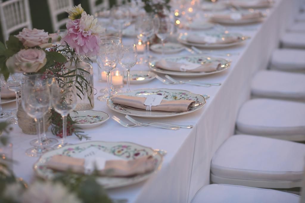 Un lungo tavolo con sopra piatti, bicchieri, tovaglioli e fiori.
