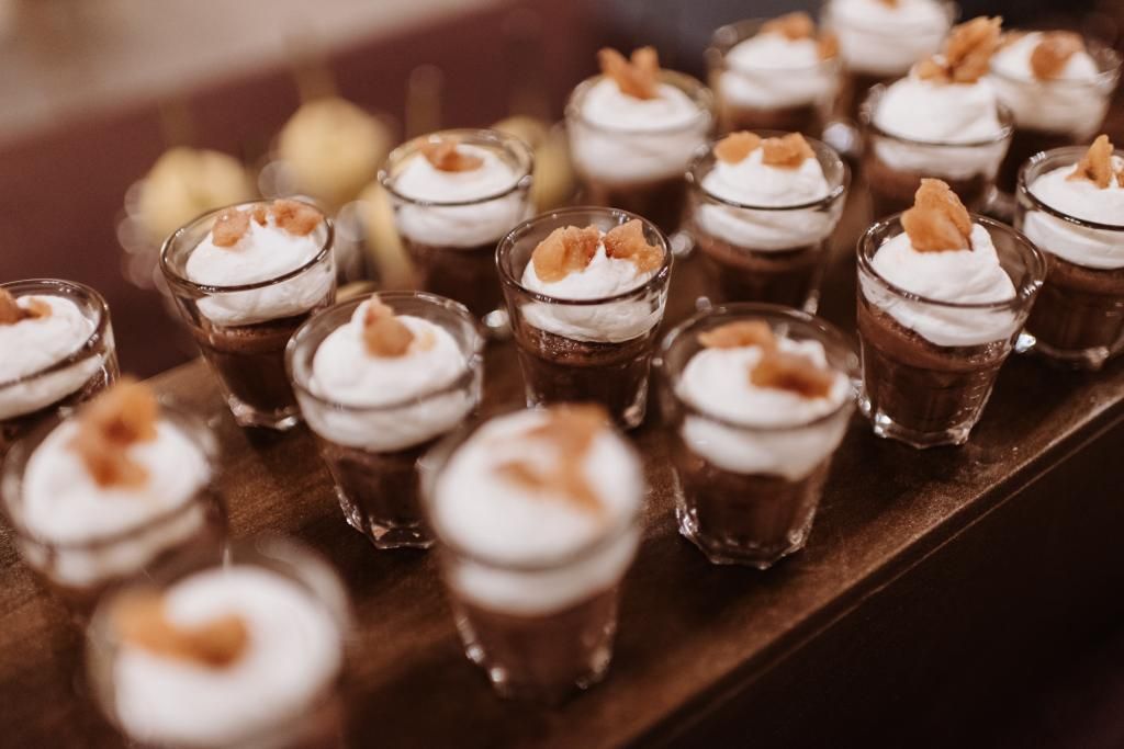 Una fila di bicchierini pieni di budino al cioccolato e panna montata.