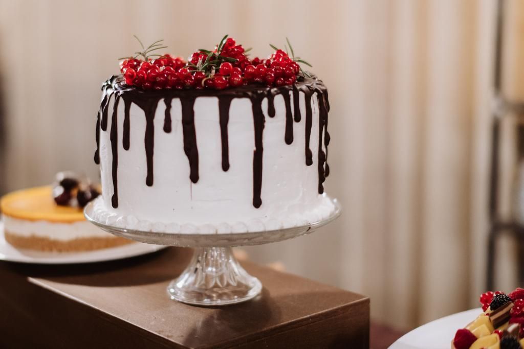 Una torta bianca con glassa al cioccolato e ribes rosso sopra è su un'alzatina su un tavolo.