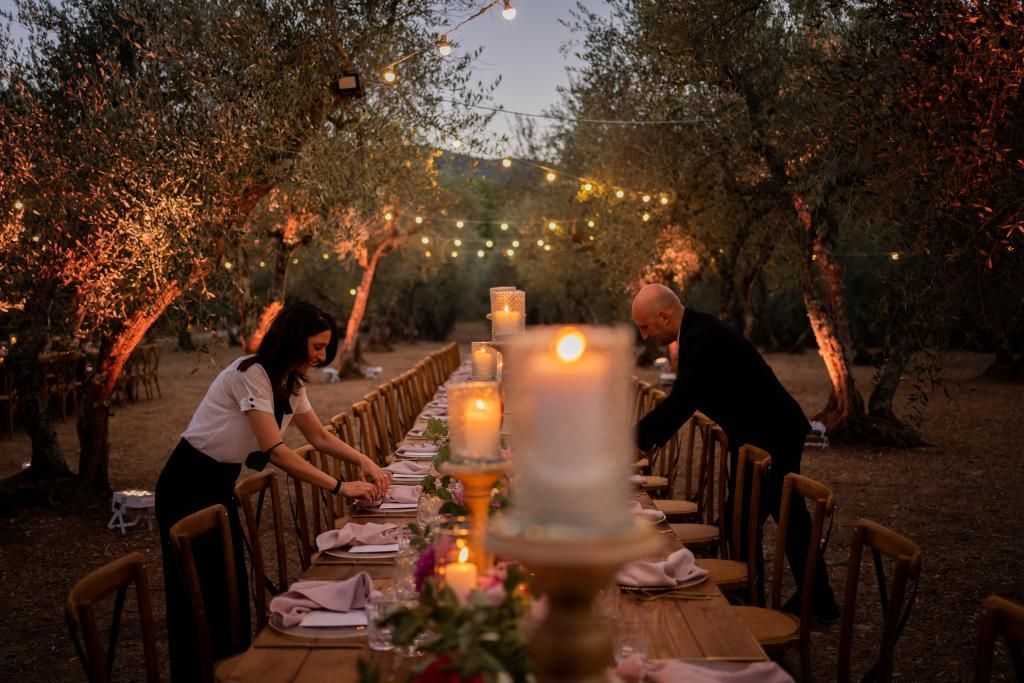 Un uomo e una donna apparecchiano una lunga tavola con le candele.