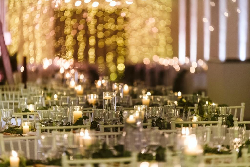 Un lungo tavolo apparecchiato per un ricevimento di nozze con candele e bicchieri.
