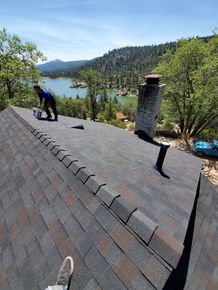 A man is working on the roof of a house overlooking a lake.