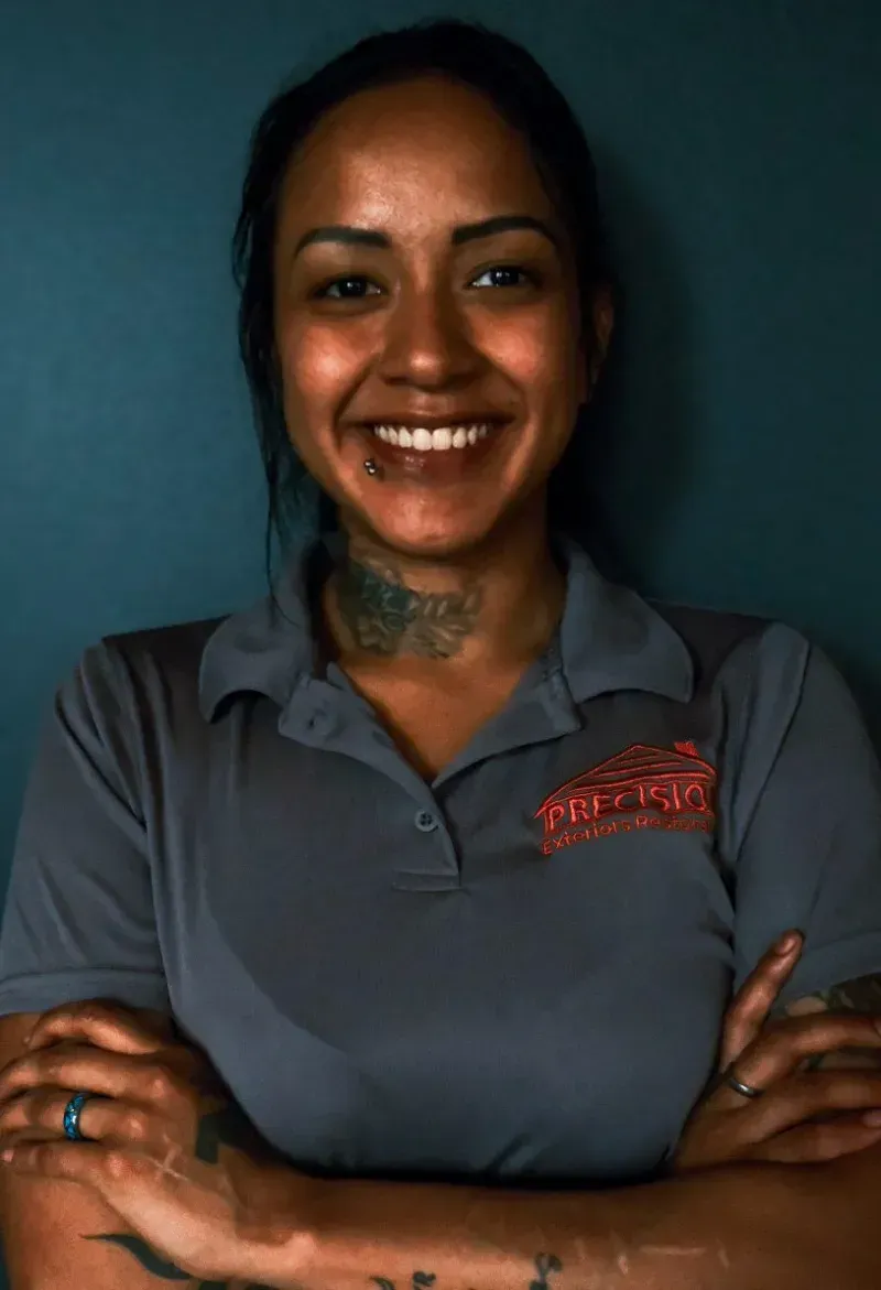 A woman with a tattoo on her neck is smiling with her arms crossed.