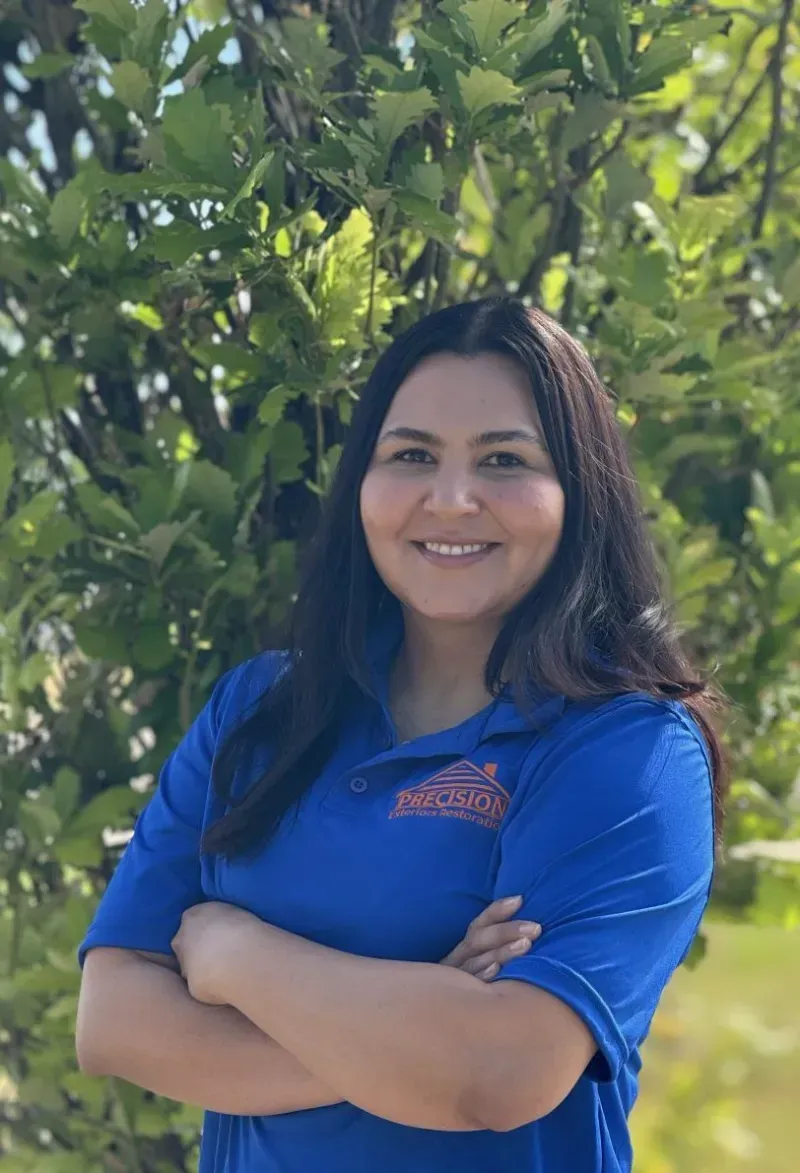 A woman in a blue shirt is posing for a picture with her arms crossed.