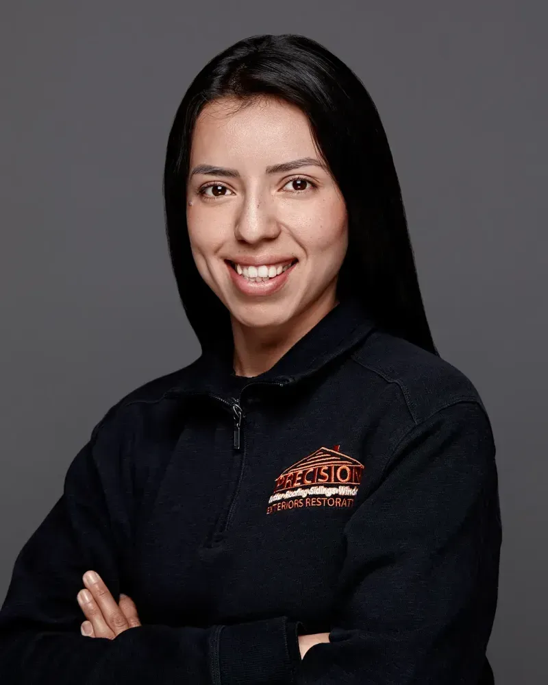 A woman in a black jacket is smiling with her arms crossed.