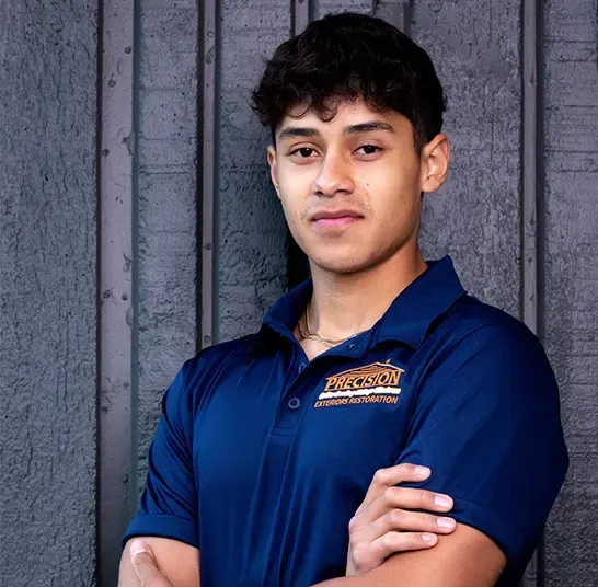 A young man in a blue shirt is standing with his arms crossed.